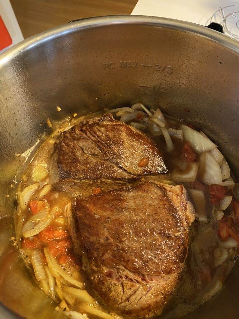 Instant Pot Chuck Roast showing seared roast in instant pot with veggies.