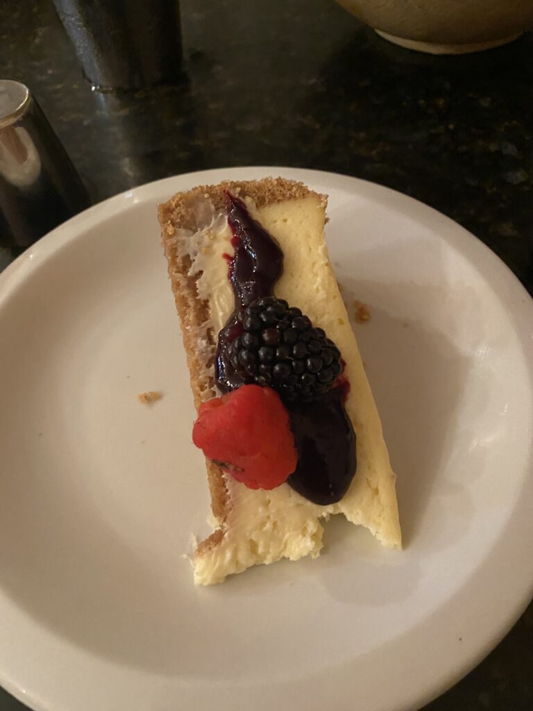 Slice of cheesecake, on a plate with raspberry puree and raspberries.