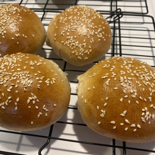 Four Homemade Sesame Seed Buns on a cooling rack