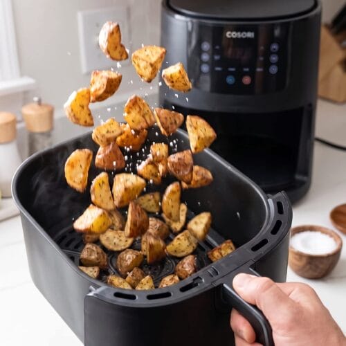 air fryer roasted potatoes being tossed with salt in the fryer basket